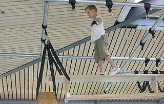 Junge balanciert unter der Hallendecke auf einer hängenden Turnbank