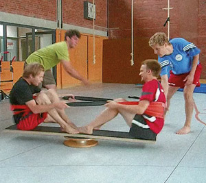 Sportstudenten an einer Bewegungsbaustelle mit Drehscheibe und Mehrzweckbrett in der Turnhalle