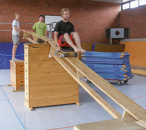 Sportstudenten an einer Bewegungsbaustelle mit Rollbahn, Rollwagen und Sprungkästen in der Turnhalle